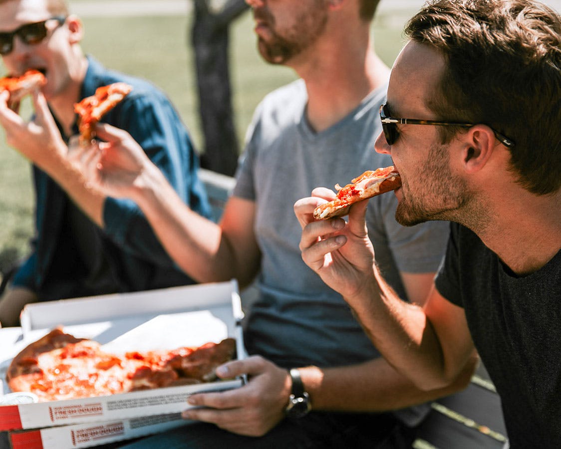A group of young men eating pizza on the grass